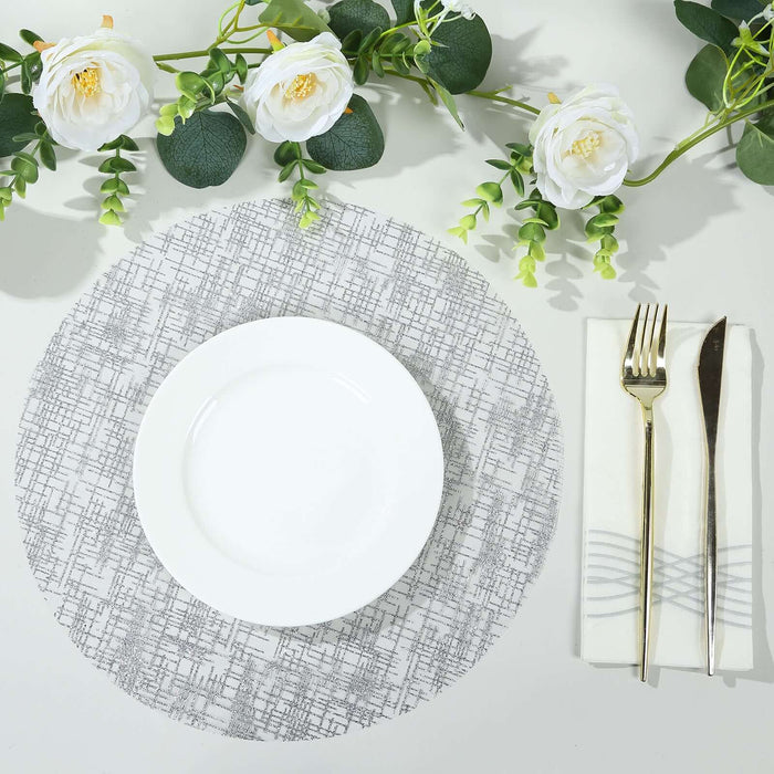 Elegant gray patterned placemat with white plate and silver cutlery, adorned with flowers.