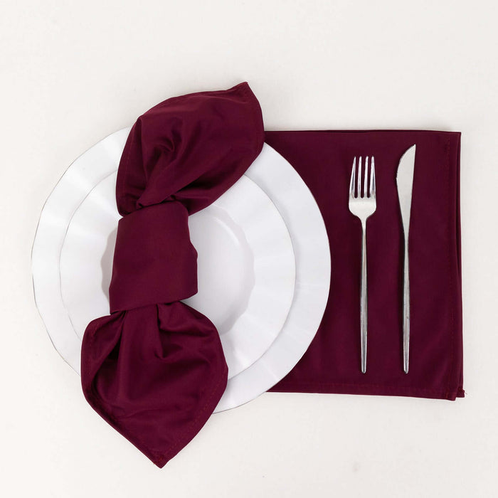 Elegant table setting with burgundy napkin, plates, and cutlery on white backdrop.