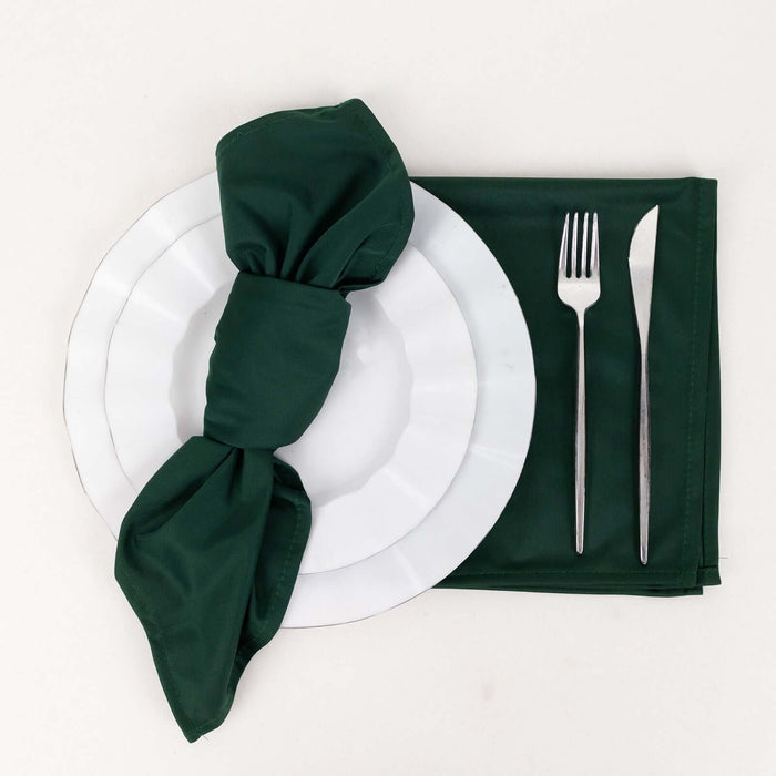 Green napkin elegantly tied on a white plate with silver cutlery on a plain backdrop.