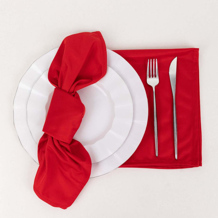 Red napkin elegantly tied on a white plate with fork and knife set.