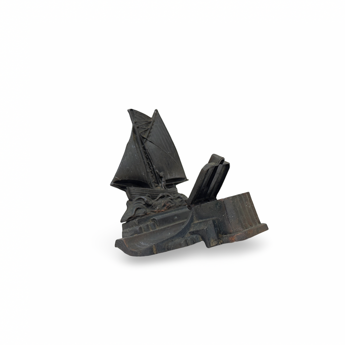 Dark metal boat inkwell with curved hull and vertical sail, antique patina