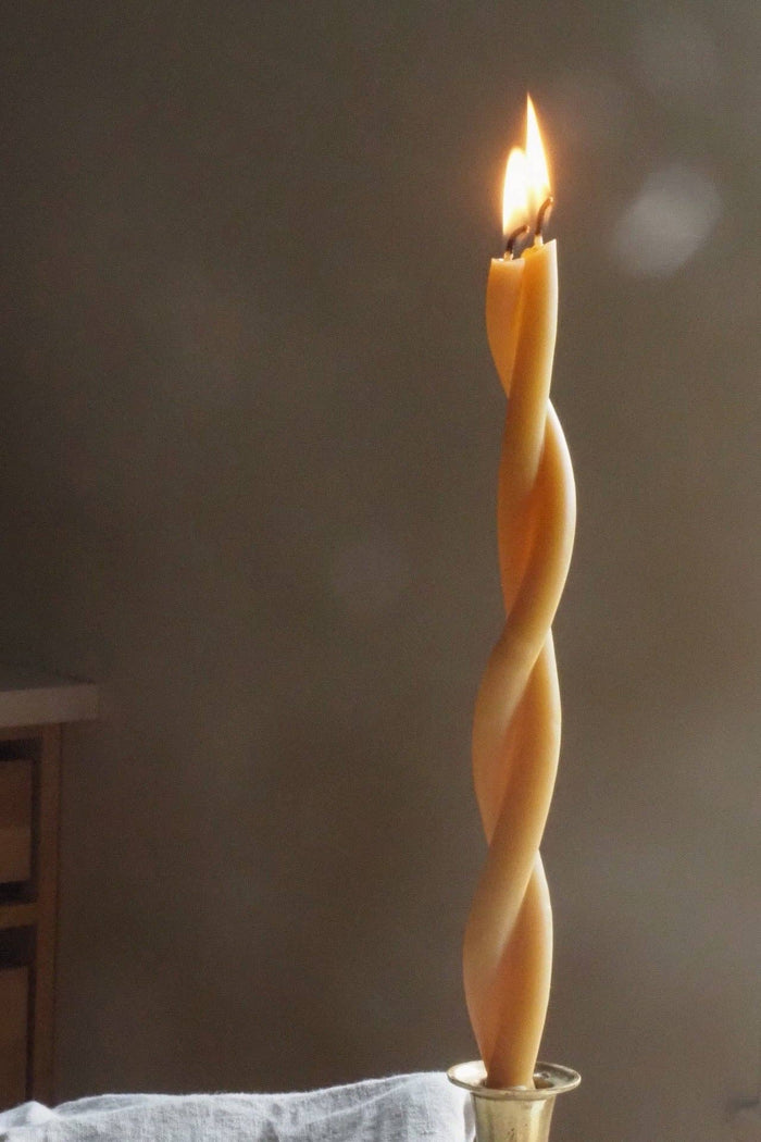 Beeswax twist taper candle with spiral ridges and lit flame, amber-gold color