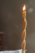 Beeswax twist taper candle with spiral ridges and lit flame, amber-gold color
