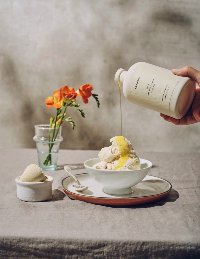 Extra virgin olive oil bottle being poured by hand into a serving bowl