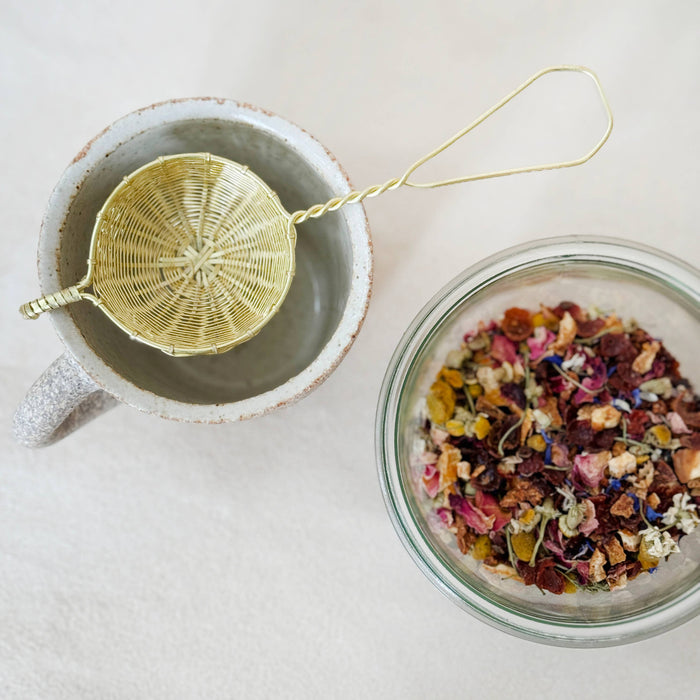 Loose herbal tea leaves in bowl and glass jar, with tea infuser