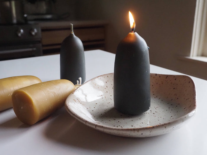 Short stub candles in dark indigo and golden, standing on a white plate