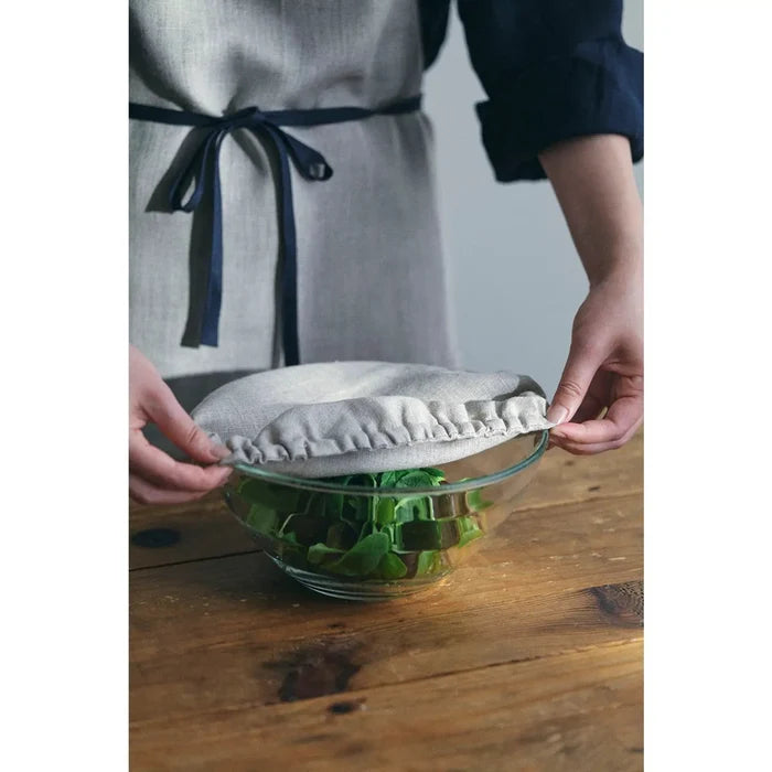 Linen bowl cover with elastic ruffle, light beige, being placed over a glass bowl