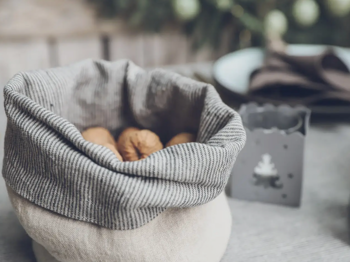 Gray striped linen storage basket with rolled rim, holding a few pinecones