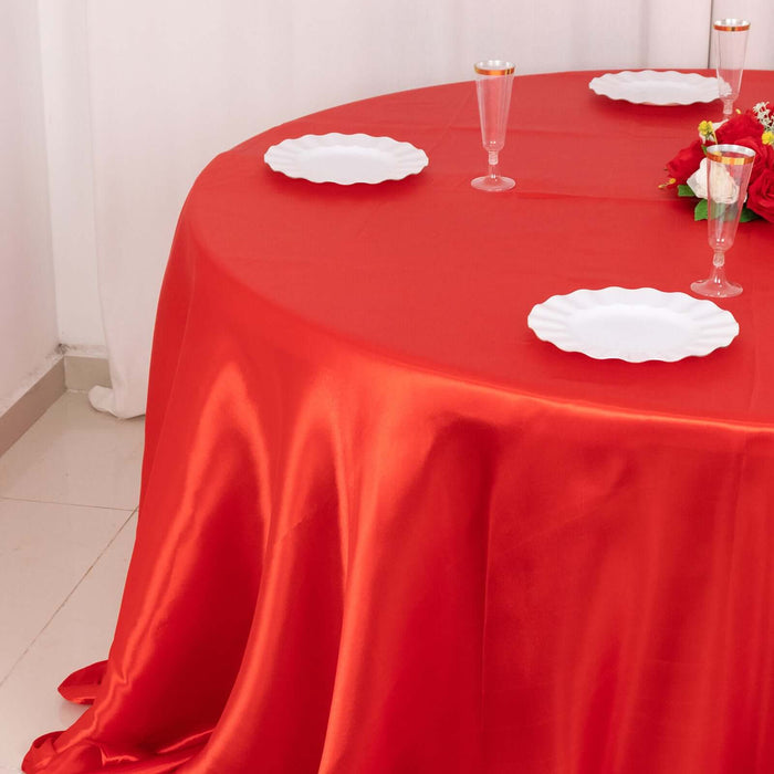 Red tablecloth draped over a round table with white plates and decorative flowers.