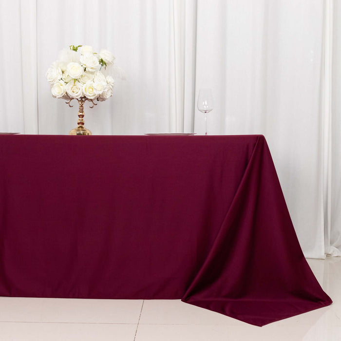 Burgundy tablecloth with floral centerpiece and wine glass on a white backdrop.