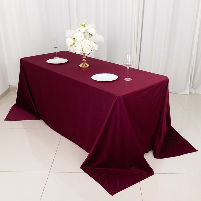 Elegant burgundy tablecloth draped over a dining table with white plates and floral centerpiece.