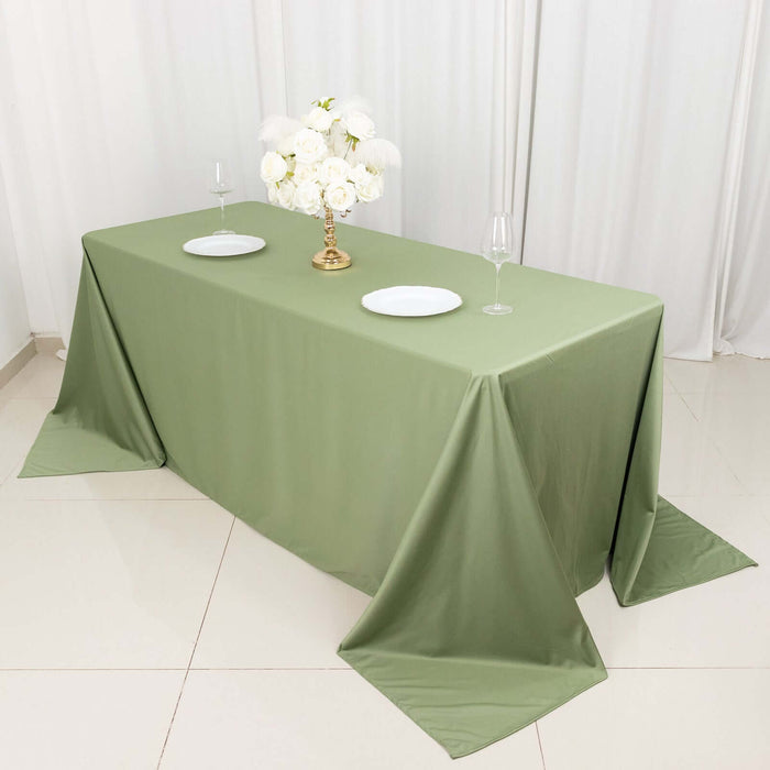 Olive green tablecloth on a dining table with decorative centerpiece and plates.