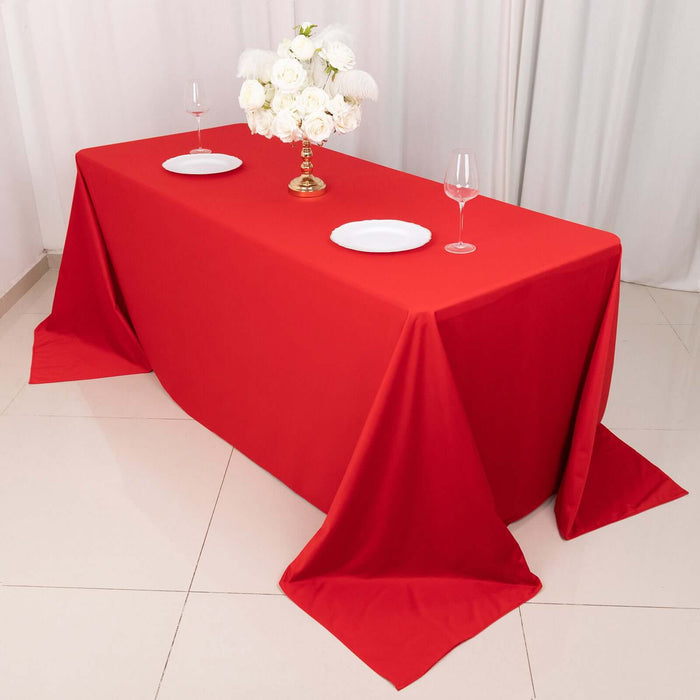 Red tablecloth draped over a table set with plates and a floral centerpiece.