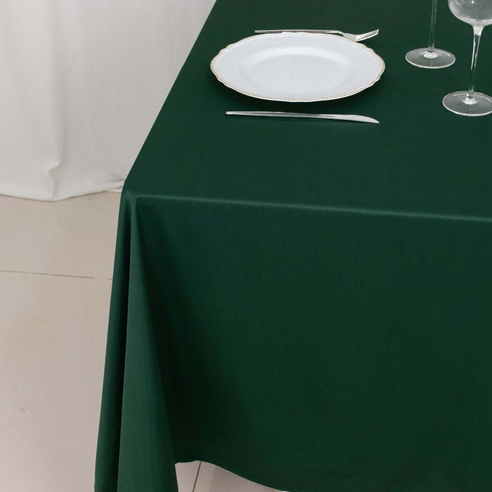 Green tablecloth with white plate and cutlery on a dining table.