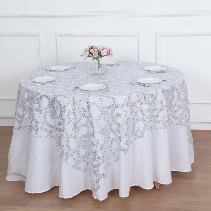 Round white tablecloth with silver floral design on a dining table.