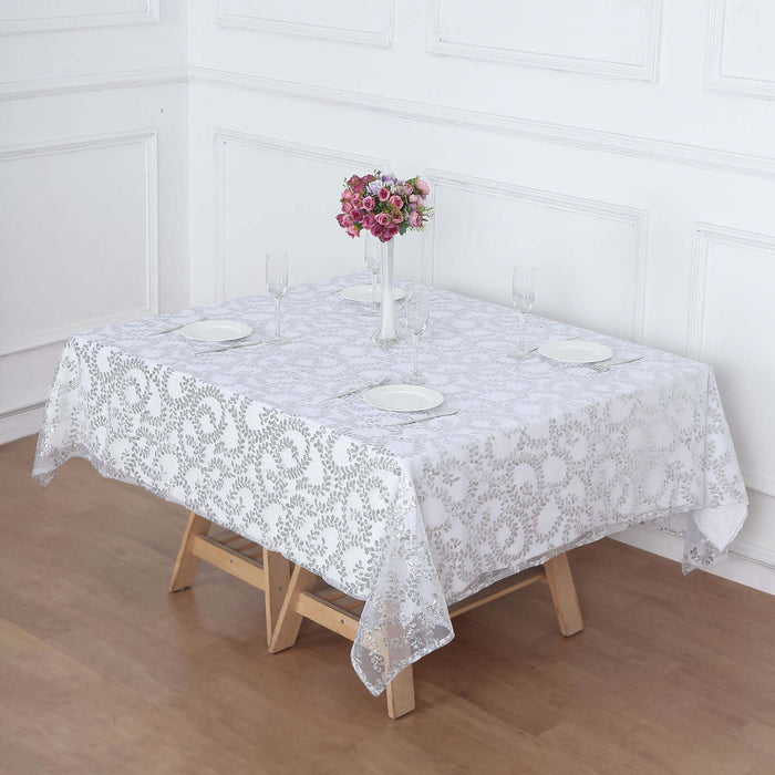 White lace tablecloth on a wooden table set for dining with flowers and plates.