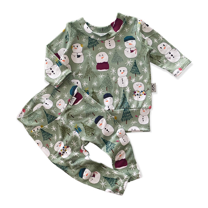 Snowman Print Lounge Set featuring a long-sleeve pullover and matching leggings with a playful snowman and winter tree design on a soft green background. Handmade for babies and toddlers, perfect for holiday celebrations and seasonal wear.