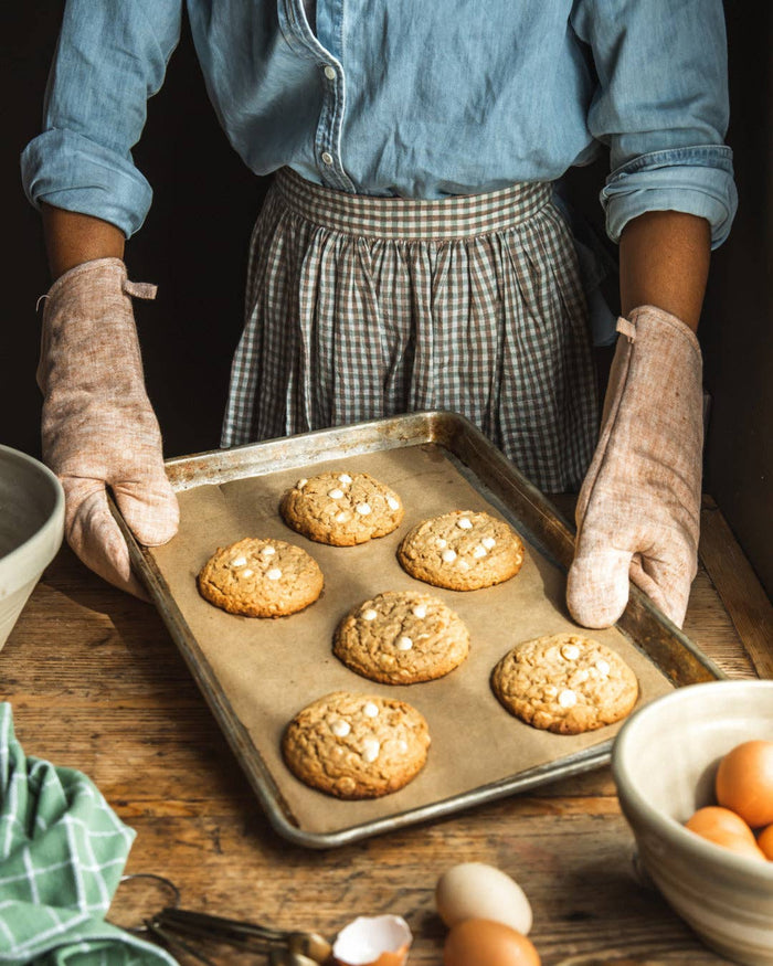 Pair of light tan linen oven mitts worn during baking, thumb and cuff visible